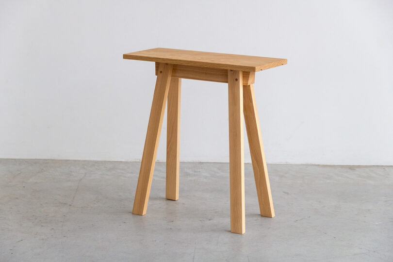 A small wooden SCP table with four angled legs stands on a smooth concrete floor against a plain white wall.
