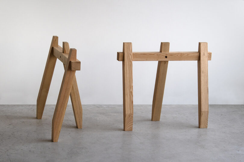 Two wooden SCP-style sawhorses with a simple, minimalist design stand on a concrete floor against a plain white background.