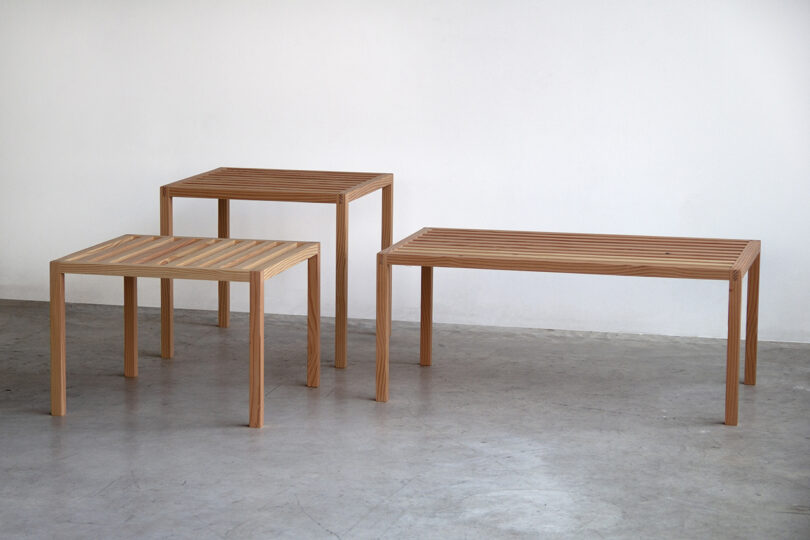 Three wooden tables of different sizes with slatted tops are arranged on a concrete floor against a plain white wall, evoking the orderly precision of an SCP containment chamber.