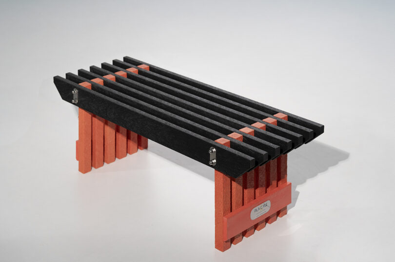 A modern bench with black slats for the seat and red block-style supports, set against a plain light background.