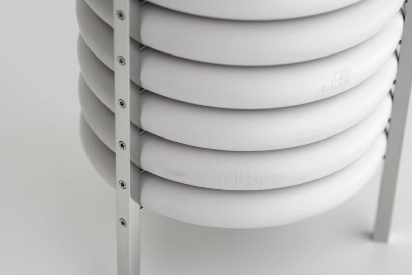 Close-up of a stack of white, circular discs held together by vertical metal rods with screws, against a plain background