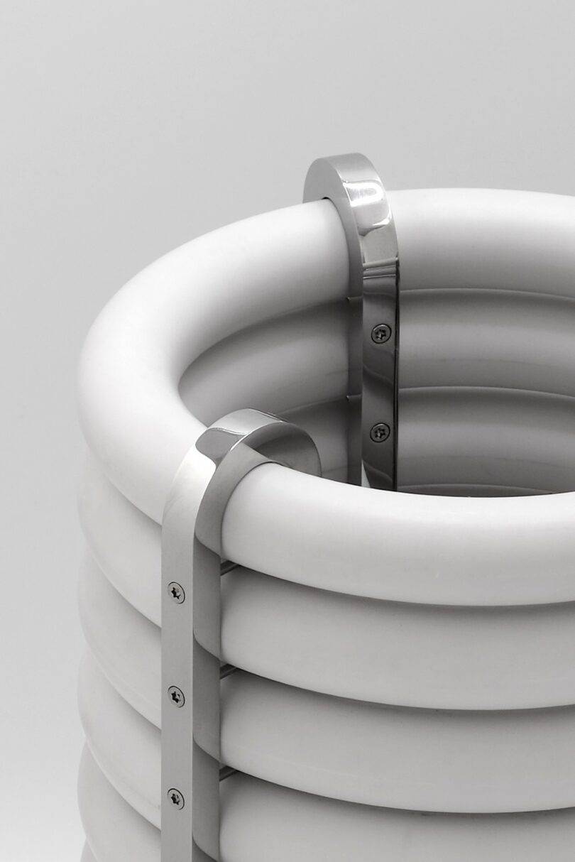 A close-up of a cylindrical object made of stacked white rings secured with vertical metal brackets and screws against a plain background