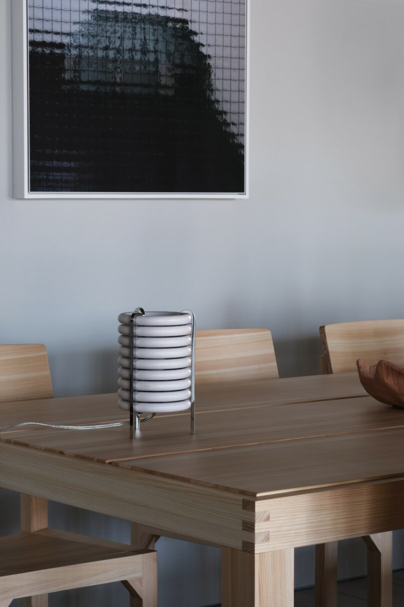 A modern wooden dining table with matching chairs, a sculptural white lamp, and a framed abstract artwork on the wall