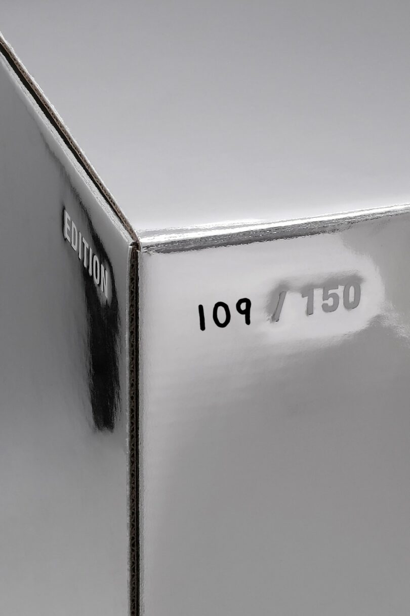 Close-up of a reflective silver box corner with "EDITION" printed on the side and "109/150" handwritten on the face