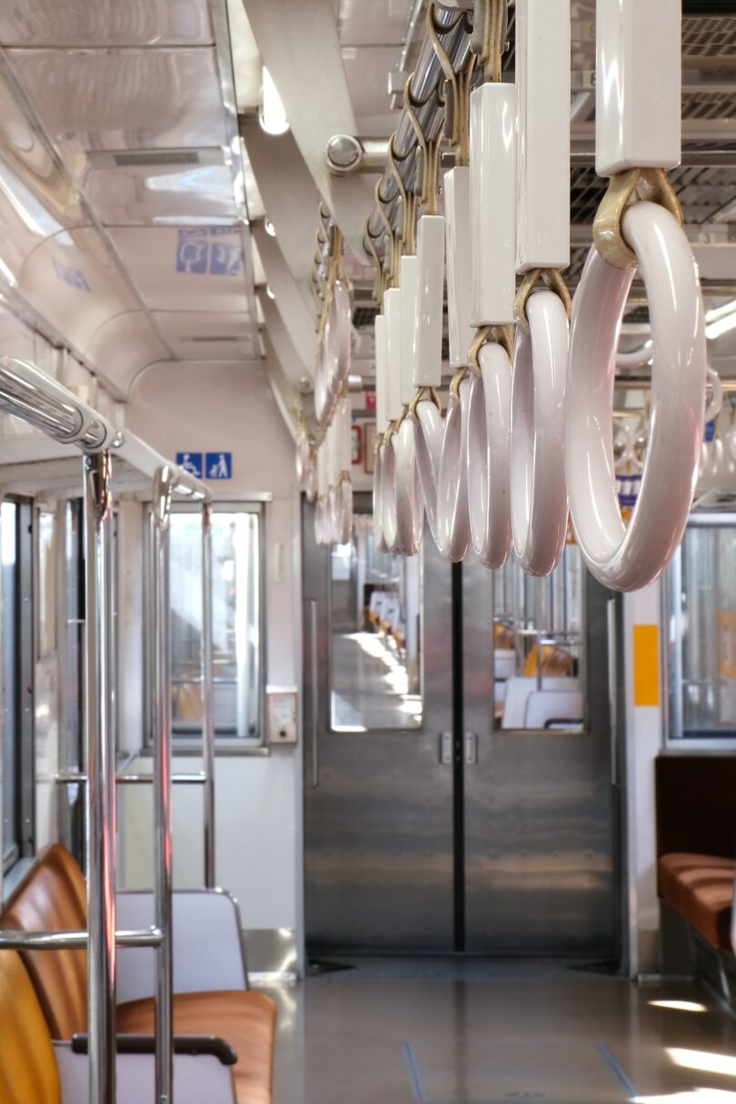 Empty train carriage with rows of brown seats and white hand straps hanging from the ceiling, facing closed double doors at the end of the car