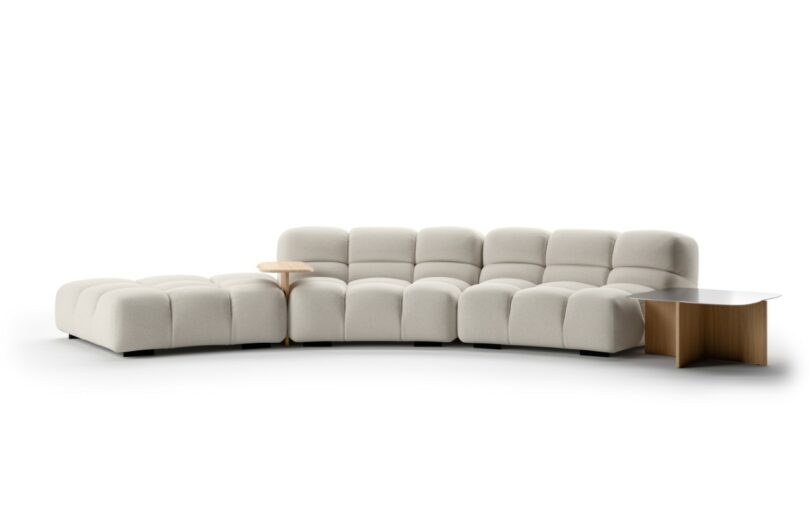 A modern, modular beige sectional sofa with tufted cushions and a built-in small wood side table.