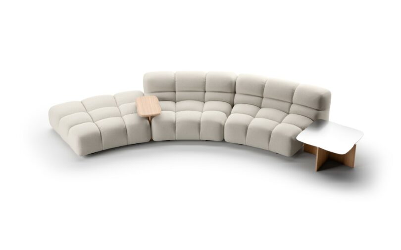 A modern, modular beige sectional sofa with tufted cushions and a built-in small wood side table.
