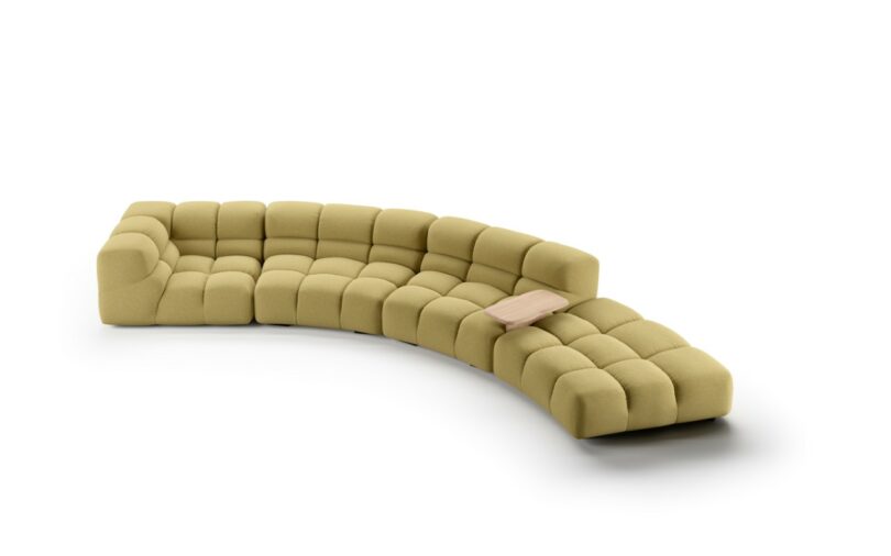 A modern, modular green sectional sofa with tufted cushions and a built-in small wood side table.