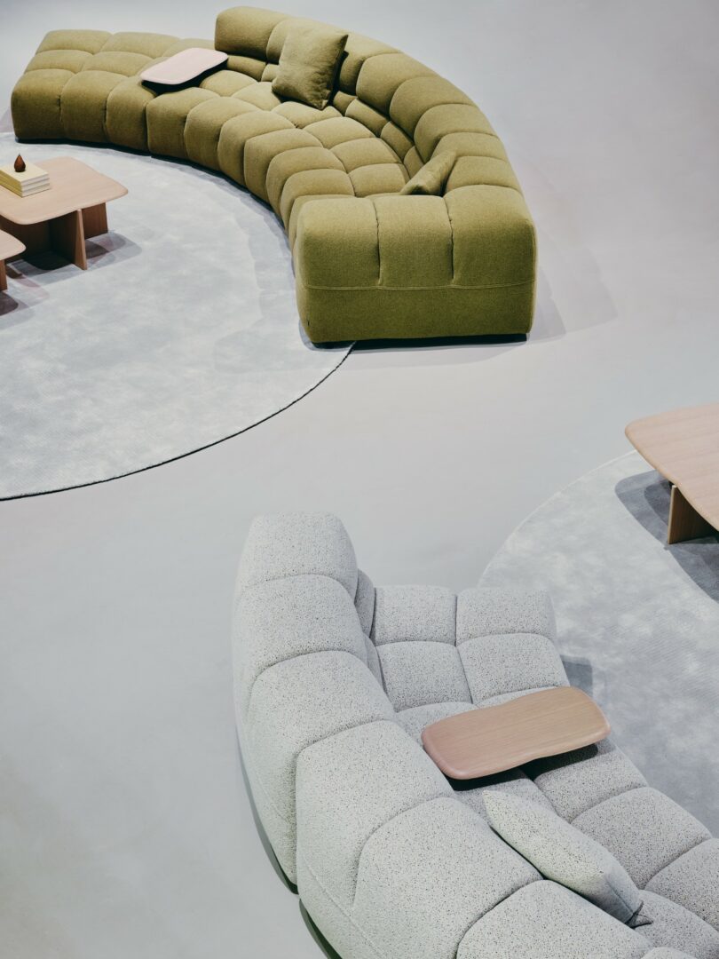 Curved modular sofas—one green, one light gray—sit on circular rugs with small wooden tables in a minimalist, open space