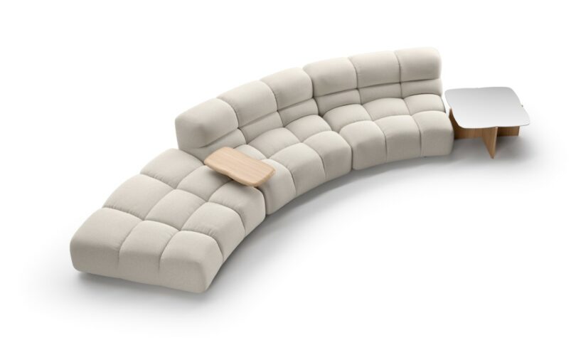 A modern, modular beige sectional sofa with tufted cushions and a built-in small wood side table and a coffee table