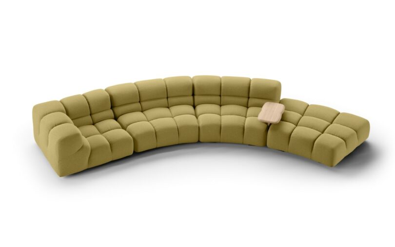 A modern, modular green sectional sofa with tufted cushions and a built-in small wood side table.