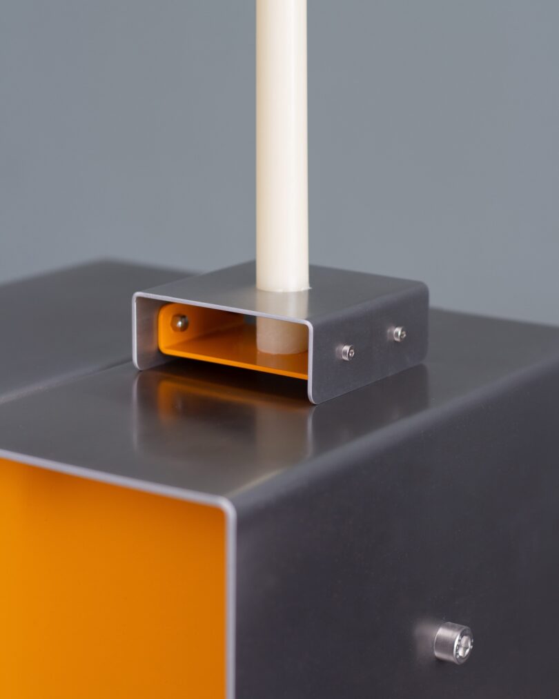 Close-up of a metal and yellow rectangular structure with a vertical white rod inserted through a metal bracket on top.