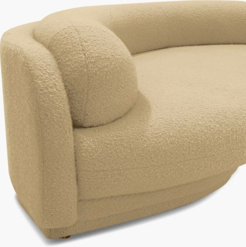 Curved beige upholstered sofa with textured fabric and a rounded armrest on one side