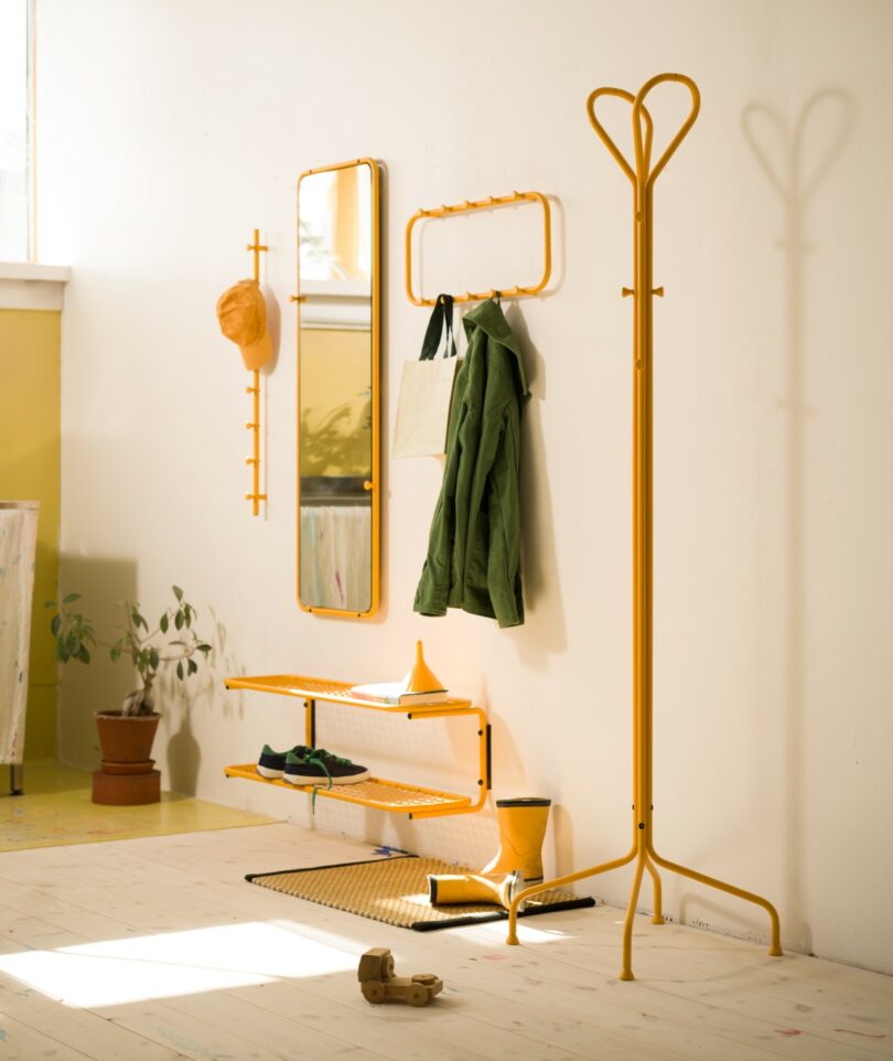 Minimalist entrance with yellow metal carrier, mirror, wall hooks, shelves, green jacket, hat, bag, rain boots and plants Utactive on white wall