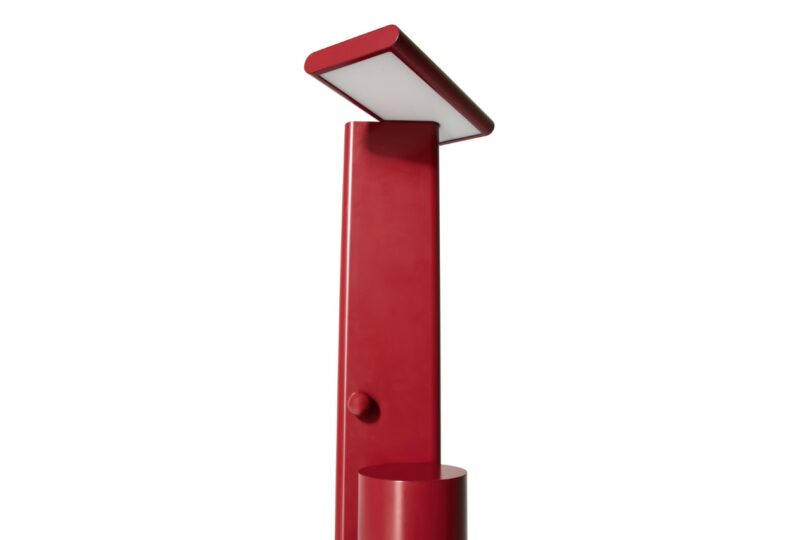 A modern, red, rectangular floor lamp with an angled flat light panel on top and a cylindrical base