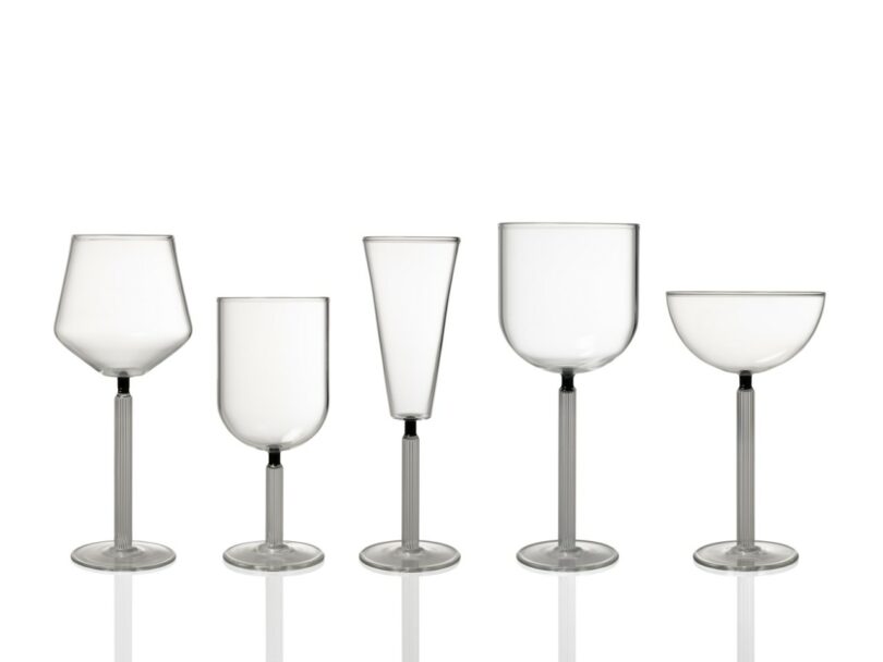 Five empty, clear glass drinkware pieces of varying shapes and sizes are arranged in a row on a white background with reflections below each glass