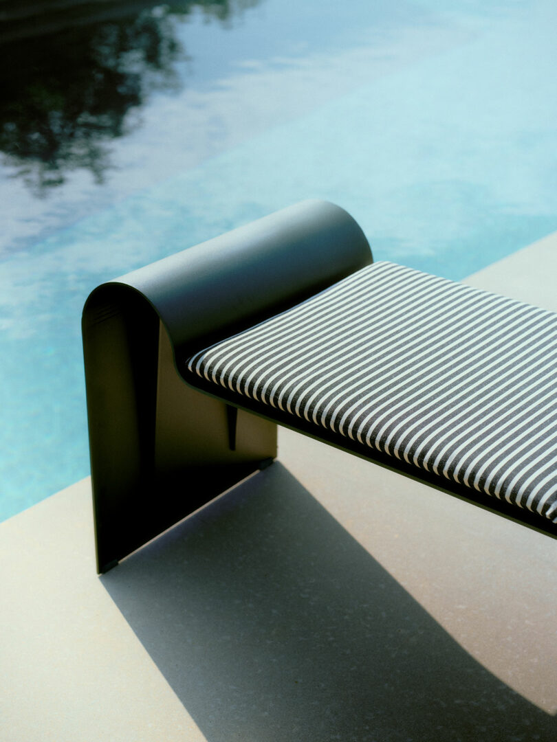 A modern outdoor bench with a black metal frame and striped cushion is positioned beside a clear swimming pool