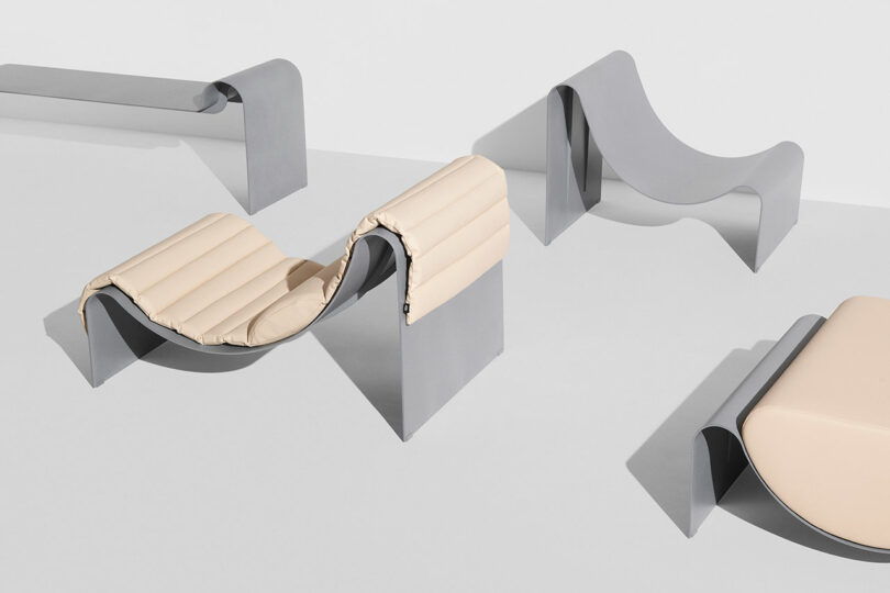 Minimalist, modern furniture pieces with curved gray metal bases and light beige cushioned seats arranged on a plain white surface