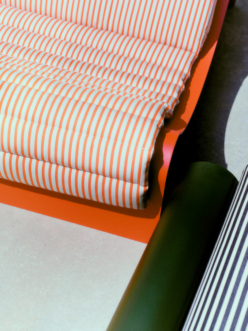 A close-up of a rolled orange and white striped fabric on an orange sheet, next to a dark green cylindrical object on a light surface