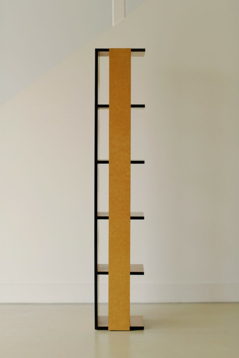 A side view of a modern, minimalist bookshelf with five shelves and a central vertical panel, standing against a plain, light-colored wall