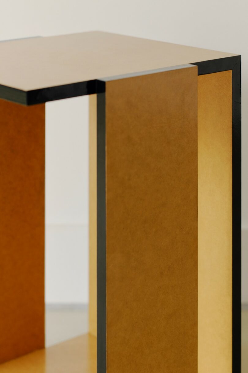 A close-up of a minimalist, rectangular wooden table or shelf with sharp black edges and a matte finish, photographed against a plain background