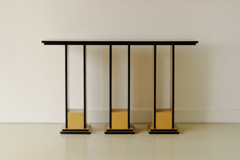 A modern console table with a dark rectangular top supported by six vertical black rods anchored to three square yellow bases