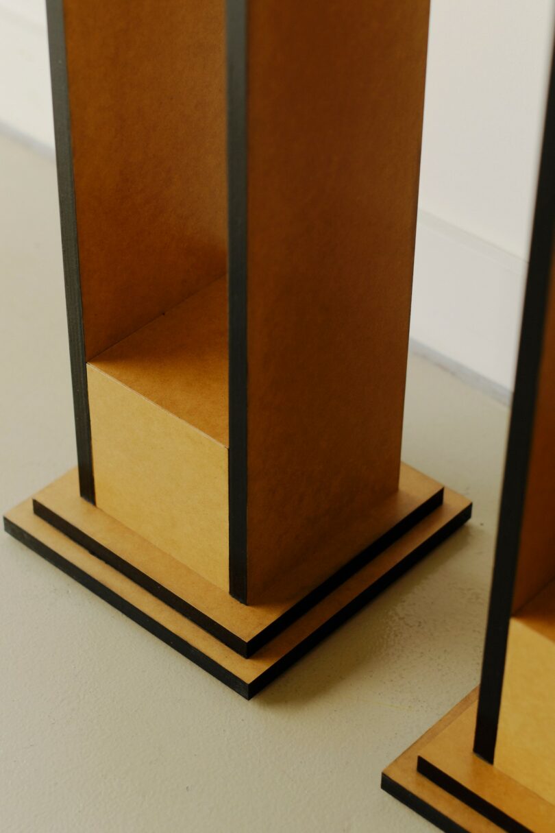 Two tall, rectangular wooden stands with black edges and layered square bases placed on a light-colored floor