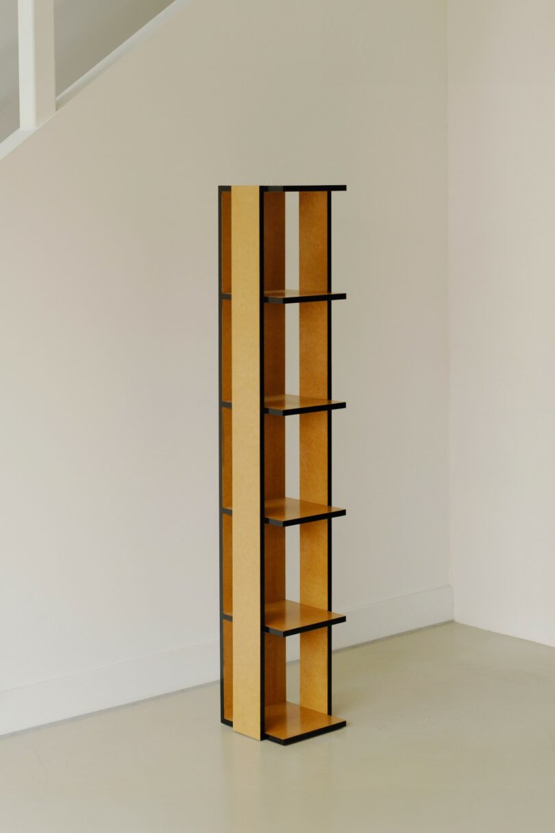 A tall, narrow shelving unit with five shelves and a minimalist design stands against a plain white wall and light floor