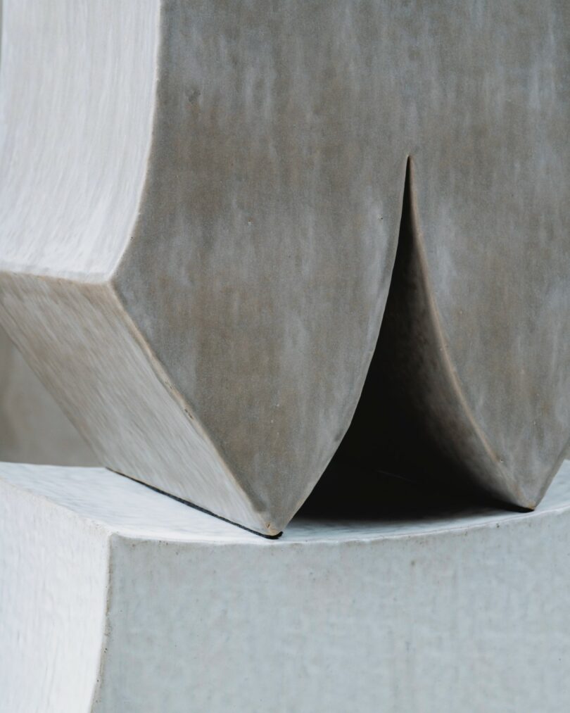 Close-up of two intersecting geometric concrete shapes with a smooth grey surface, featuring angular edges and a deep central crease or groove