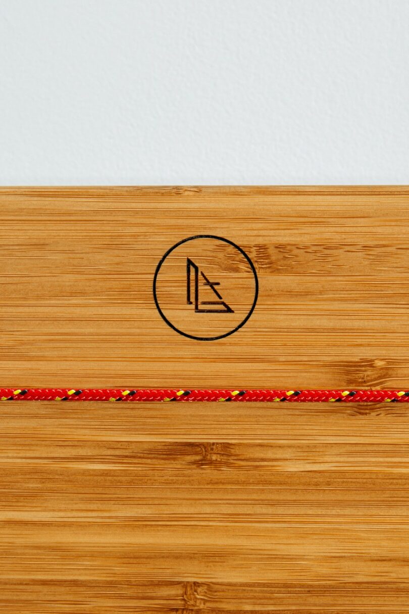 A wooden surface with a black geometric logo in a circle and a red and yellow braided cord running horizontally across it