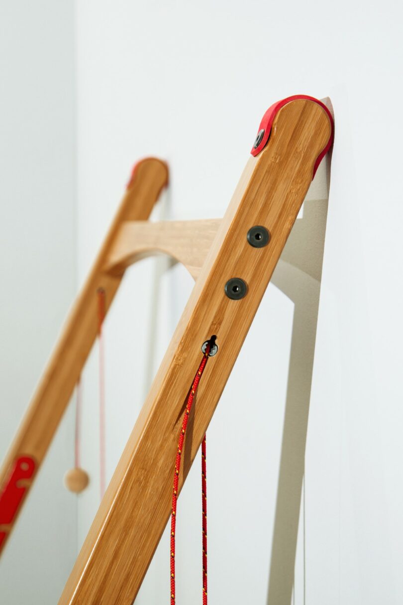 A close-up of a wooden desk with red accents and cords, leaning against a white wall