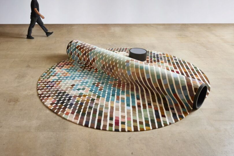 A person walks towards a bench-carpet hybrid, with a small round table nearby in a spacious room