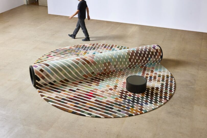 A person walks away from a bench-carpet hybrid, with a small round table nearby in a spacious room