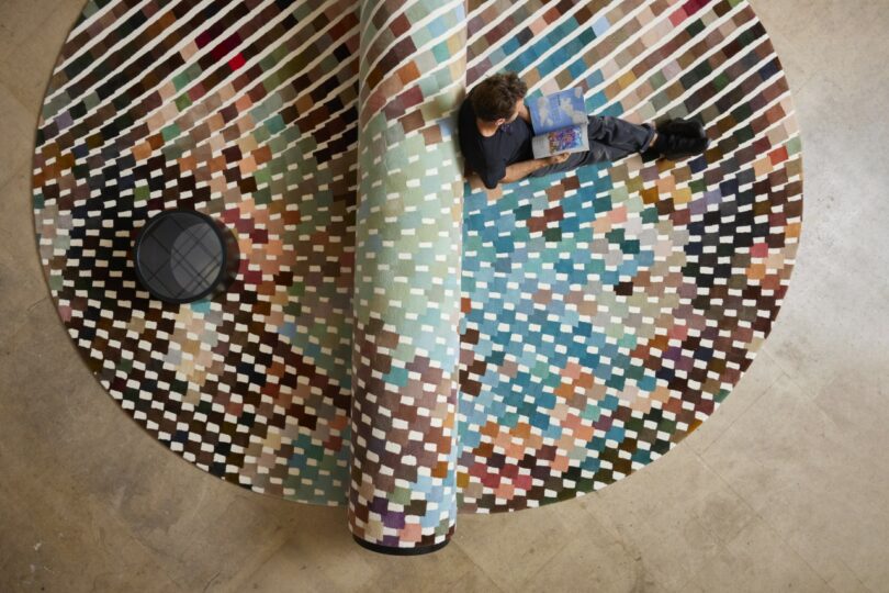 A person reads a book while lying on a large bench-carpet hybrid