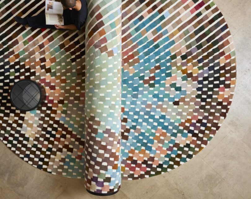 A person reads a book while lying on a large bench-carpet hybrid