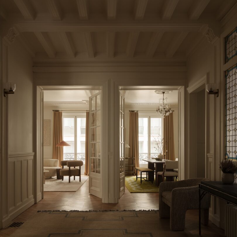 A warmly lit hallway opens into two adjacent rooms with large windows, neutral furnishings, a chandelier, and wooden floors.
