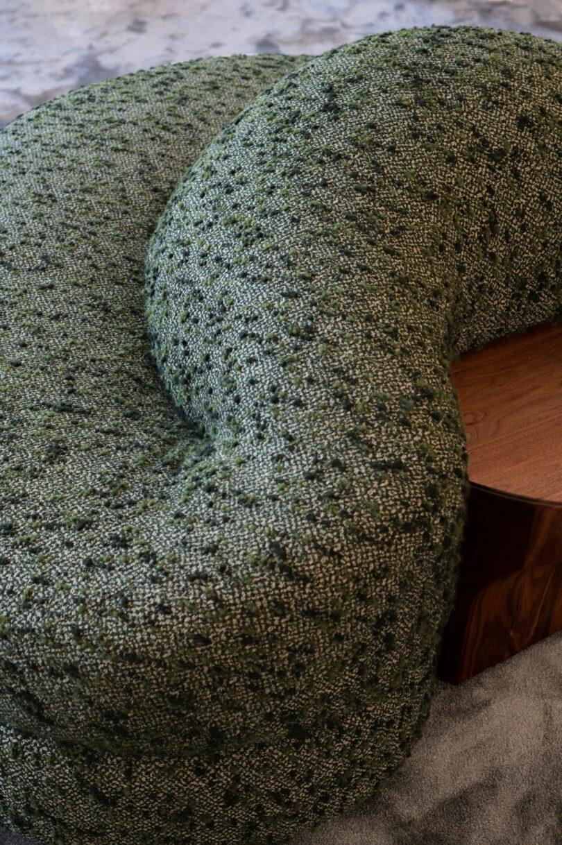 Curved, green textured fabric sofa with a wooden side table on a gray carpeted floor
