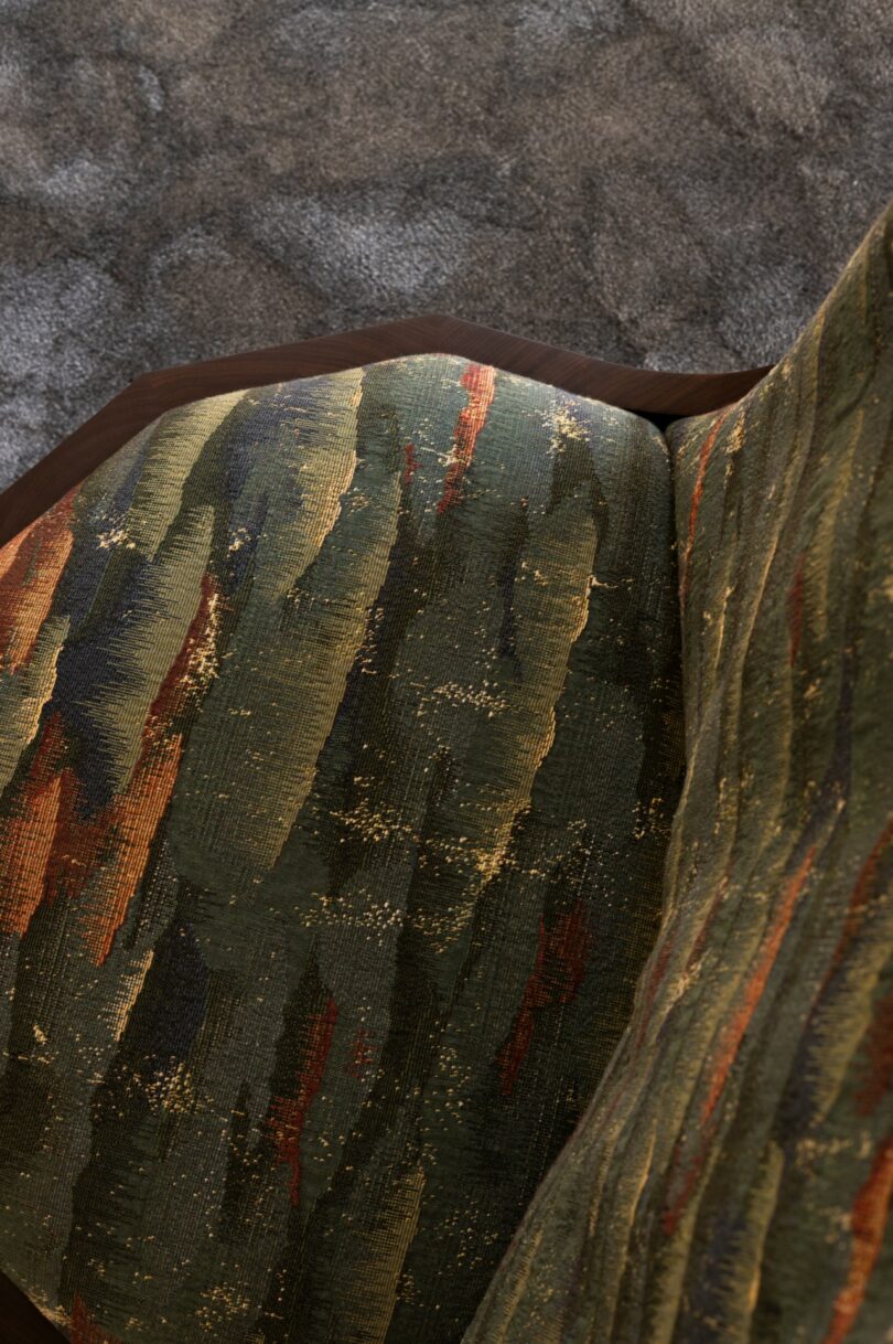 Close-up of an upholstered chair with a green, gold, and orange abstract pattern, positioned on a textured gray carpet
