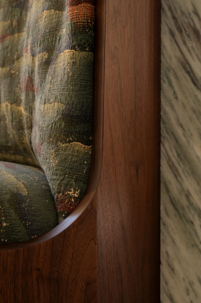 Close-up of a wooden chair with a multicolored patterned fabric cushion next to a wall with a green and white marble texture