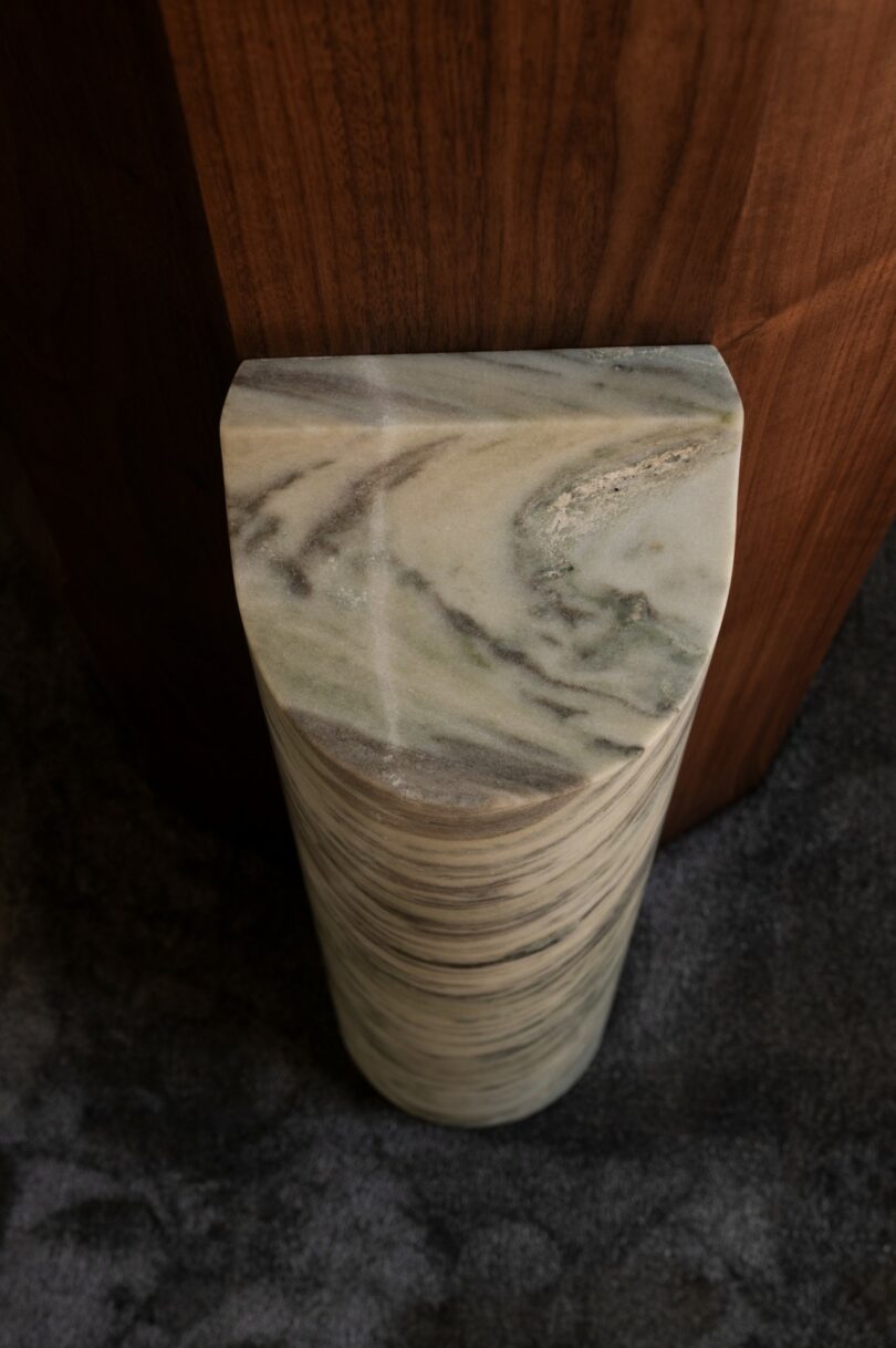 A polished, half-cylinder column of green and white marble stands on a gray carpet next to a wooden surface