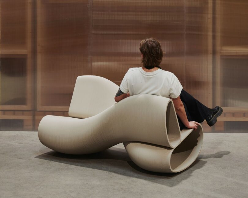 person sitting on A sculptural, beige-colored bench with a twisting, wave-like design