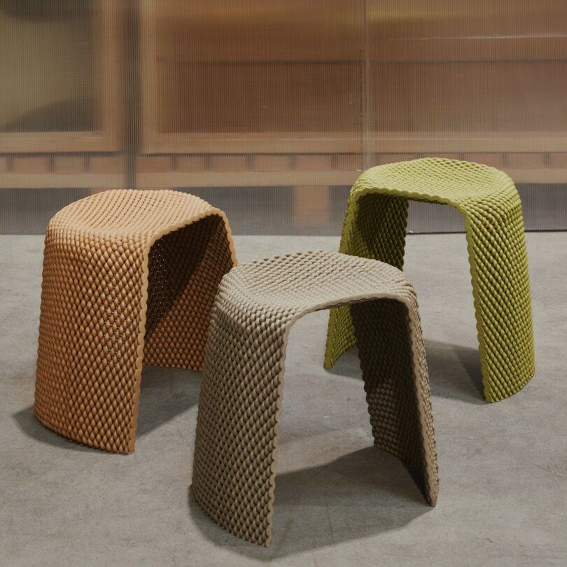 Three textured stools in orange, green, and beige colors sit on a concrete floor
