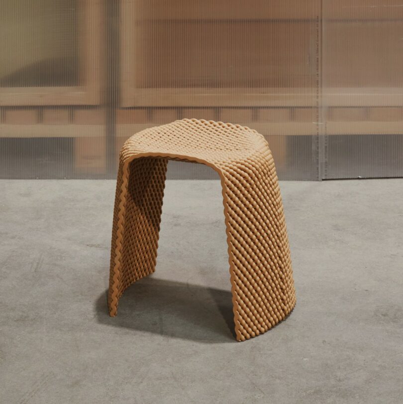A textured, orange stool placed on a concrete floor in front of a translucent partition.