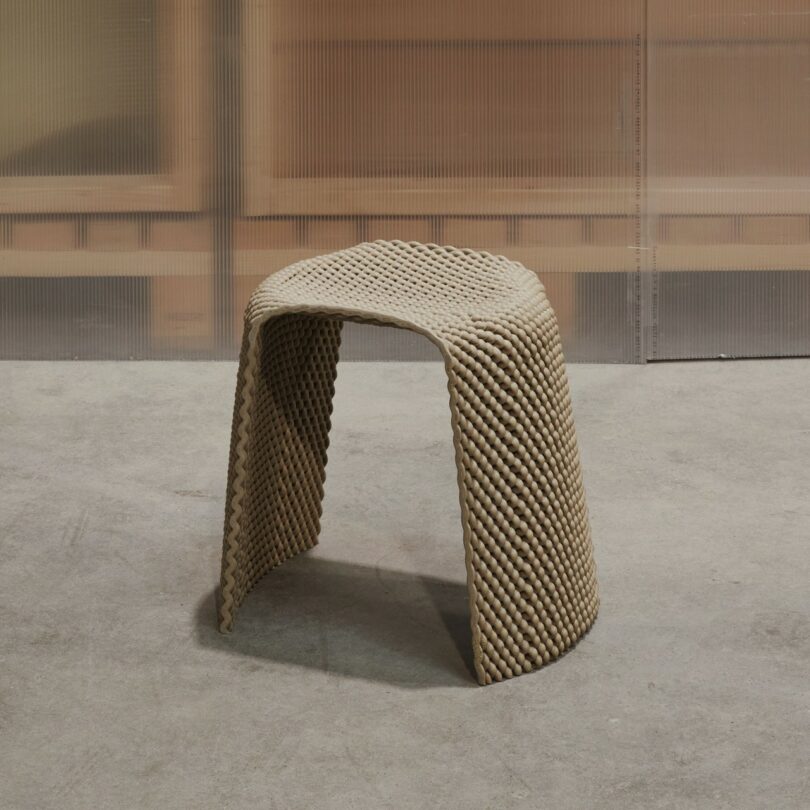 A textured, grey stool placed on a concrete floor in front of a translucent partition.