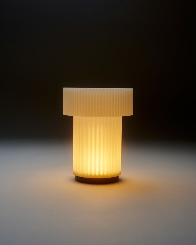 A cylindrical, ribbed lamp emits a warm yellow light, illuminating the surface beneath it against a dark background