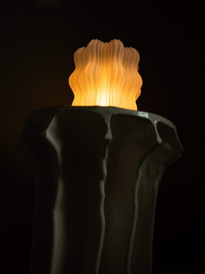 A sculpted, glowing yellow flame atop a white, textured pedestal against a dark background