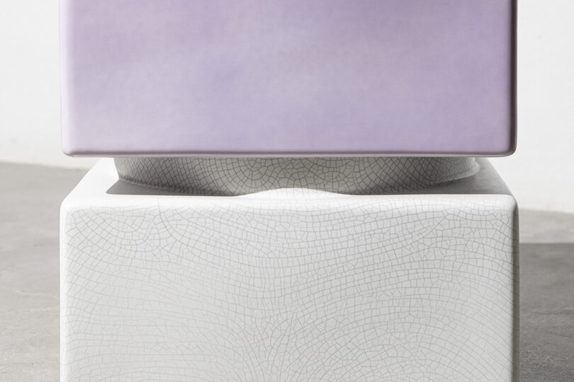 A smooth, light purple rectangular block sits on top of a white rectangular block with a cracked texture and a slight depression on its surface.