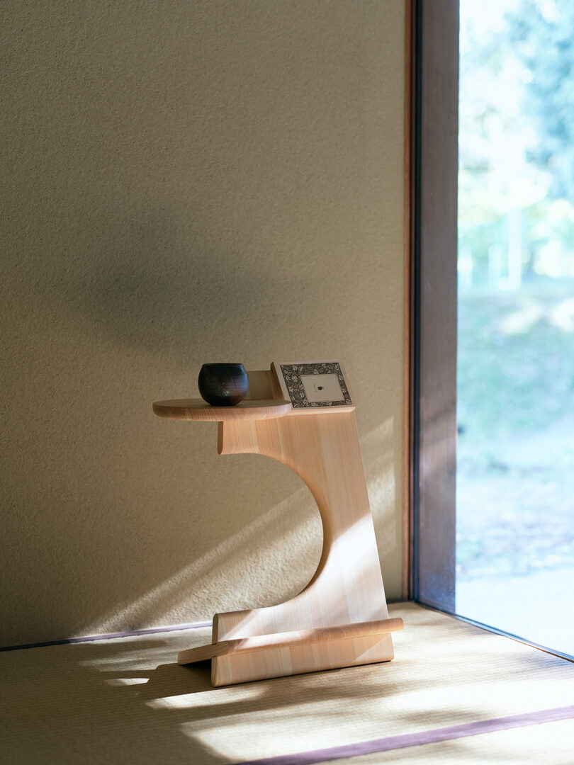 A small wooden stand holds a ceramic cup and a framed photograph, placed by a sunlit window on a tatami mat floor.