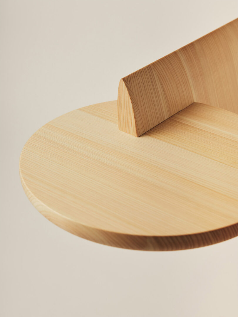 A round wooden shelf with light wood grain, attached to a vertical wooden support against a neutral background.