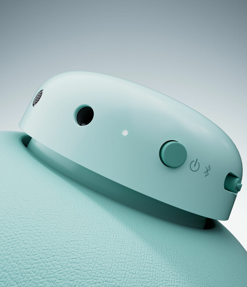 Close-up view of the top section of a teal electronic device featuring a power button, a small indicator light, and a textured surface.